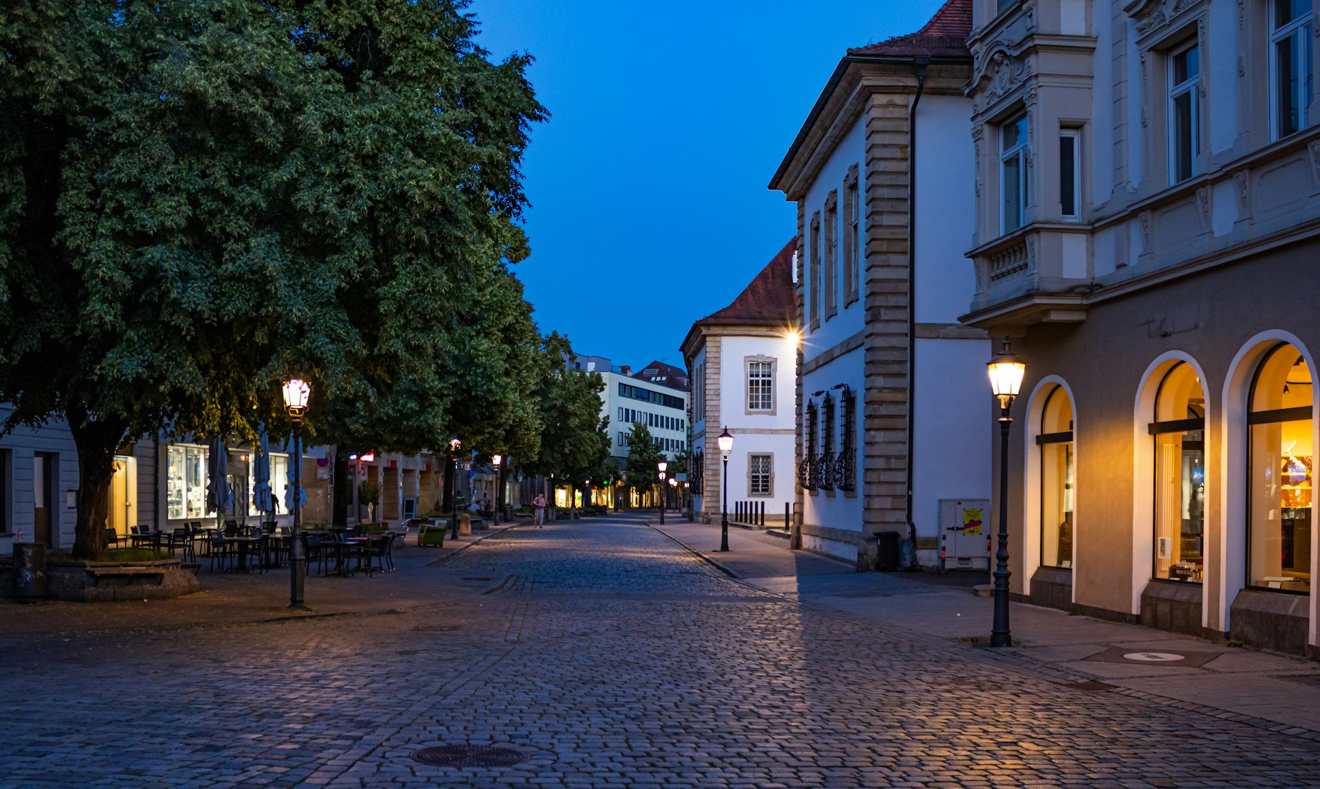 A cobblestone European street glowing under lanterns at twilight